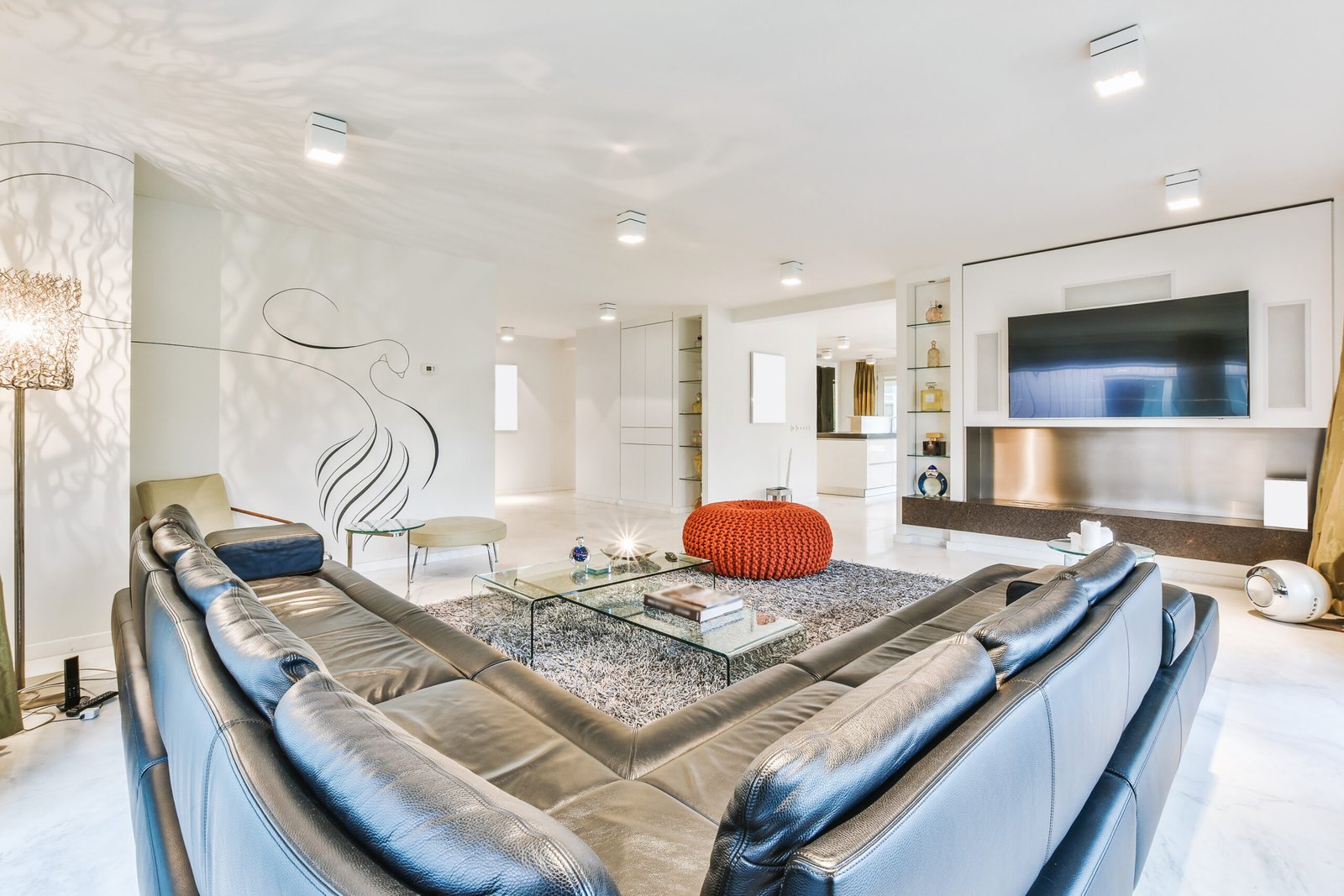 Leather corner couch located near glass tables and knitted pouf in spacious modern living room